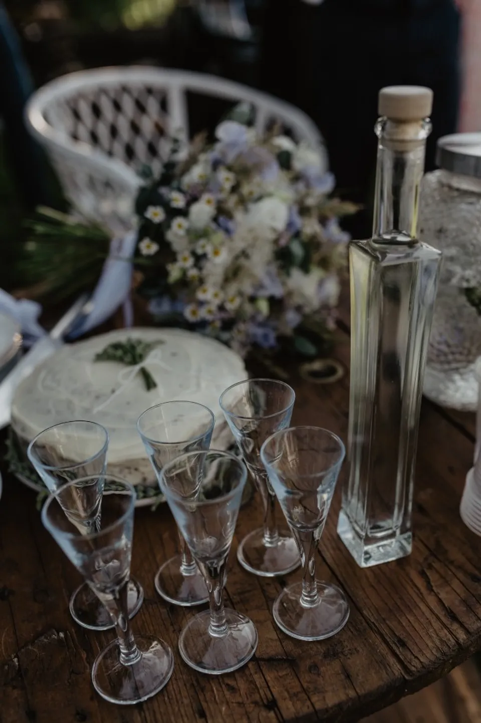 Rustic wedding table with cake, stemmed glasses and a carafe on dark wood