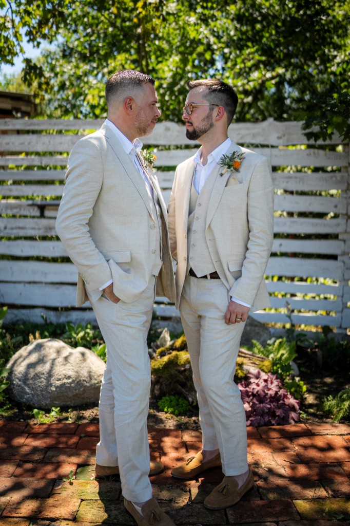 Grooms face to face on a brick patio by a white wooden fence
