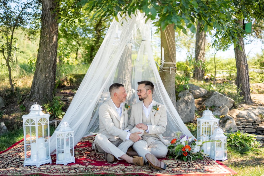 Couple seated under a white canopy on a patterned rug among trees
