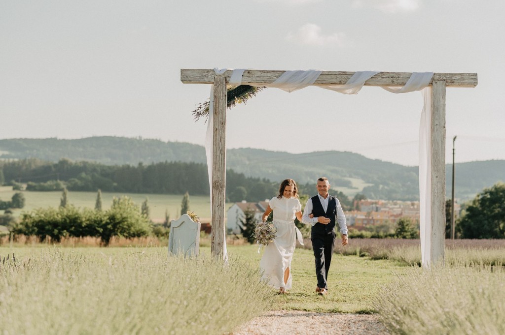 Newlyweds walking from the wooden wedding arch through the lavender rows