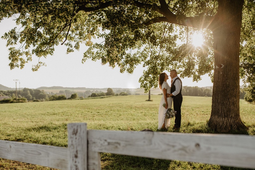 Newlyweds under a large tree at sunset on the farm