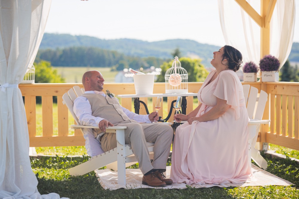 Newlyweds in a wooden gazebo with sparkling wine, countryside view