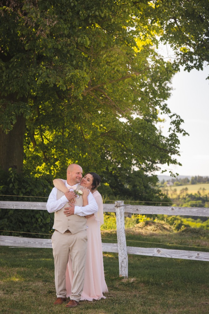 Embrace by a white wooden fence with rolling green hills