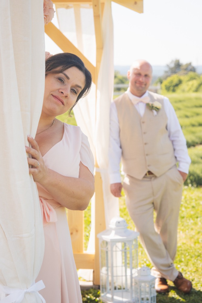 Bride peeking from a white drape, groom softly in the background
